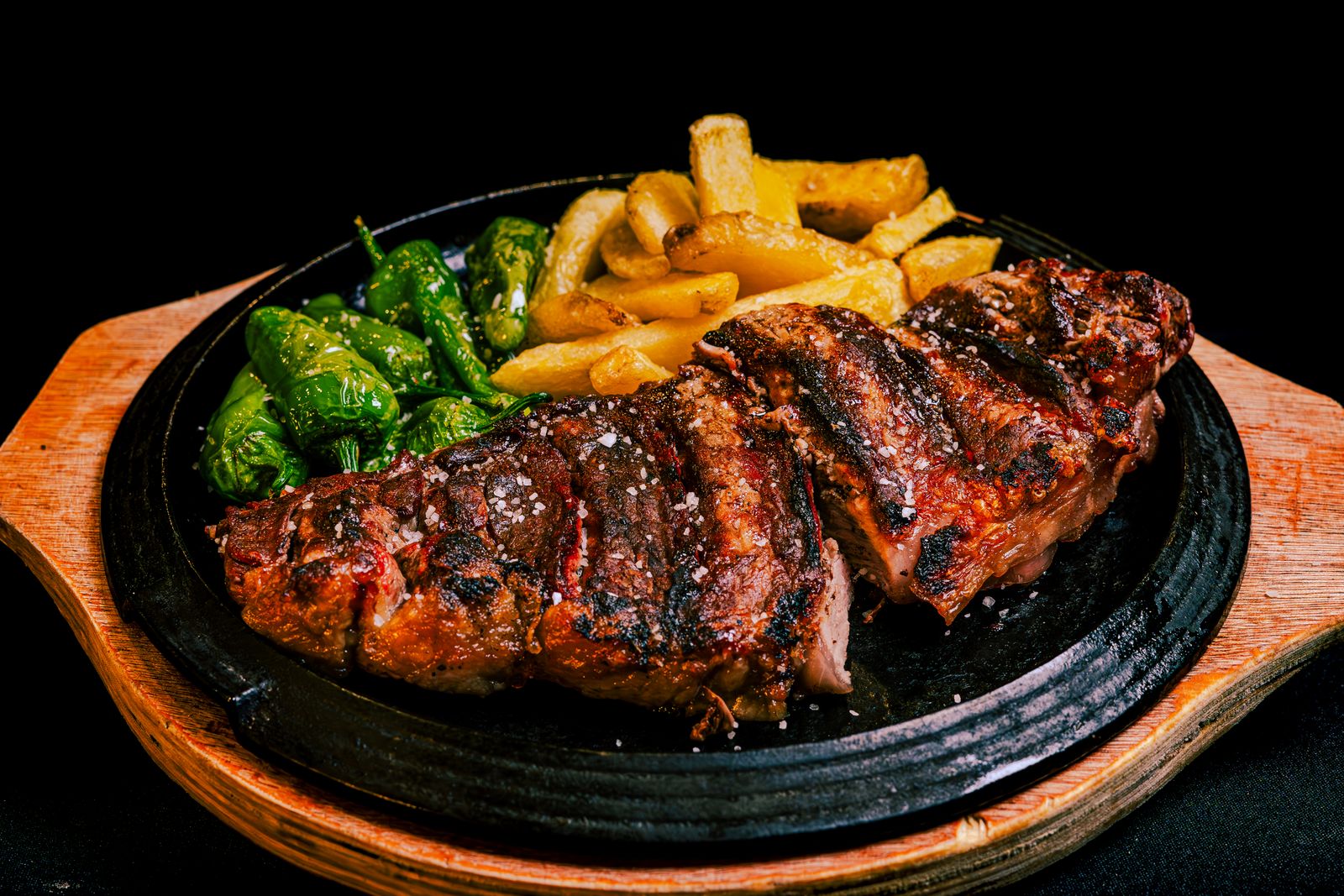 Grilled steak with fries and green peppers on a black plate