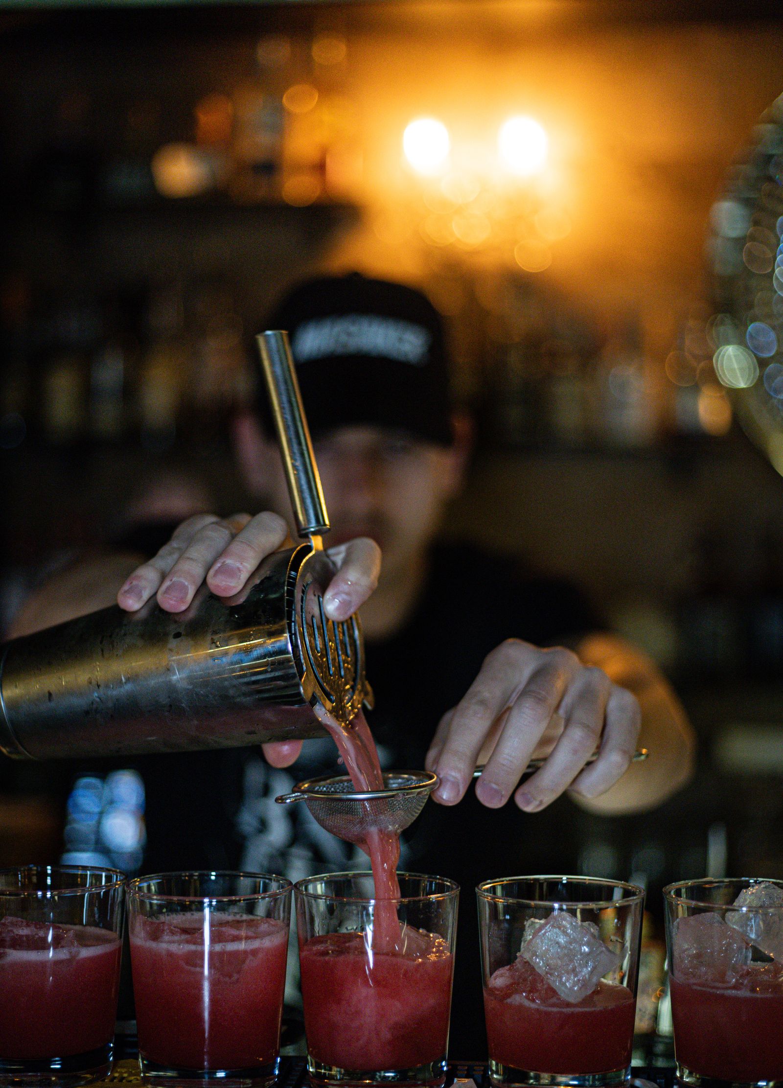 Bartender straining a round of red cocktails at a dim bar